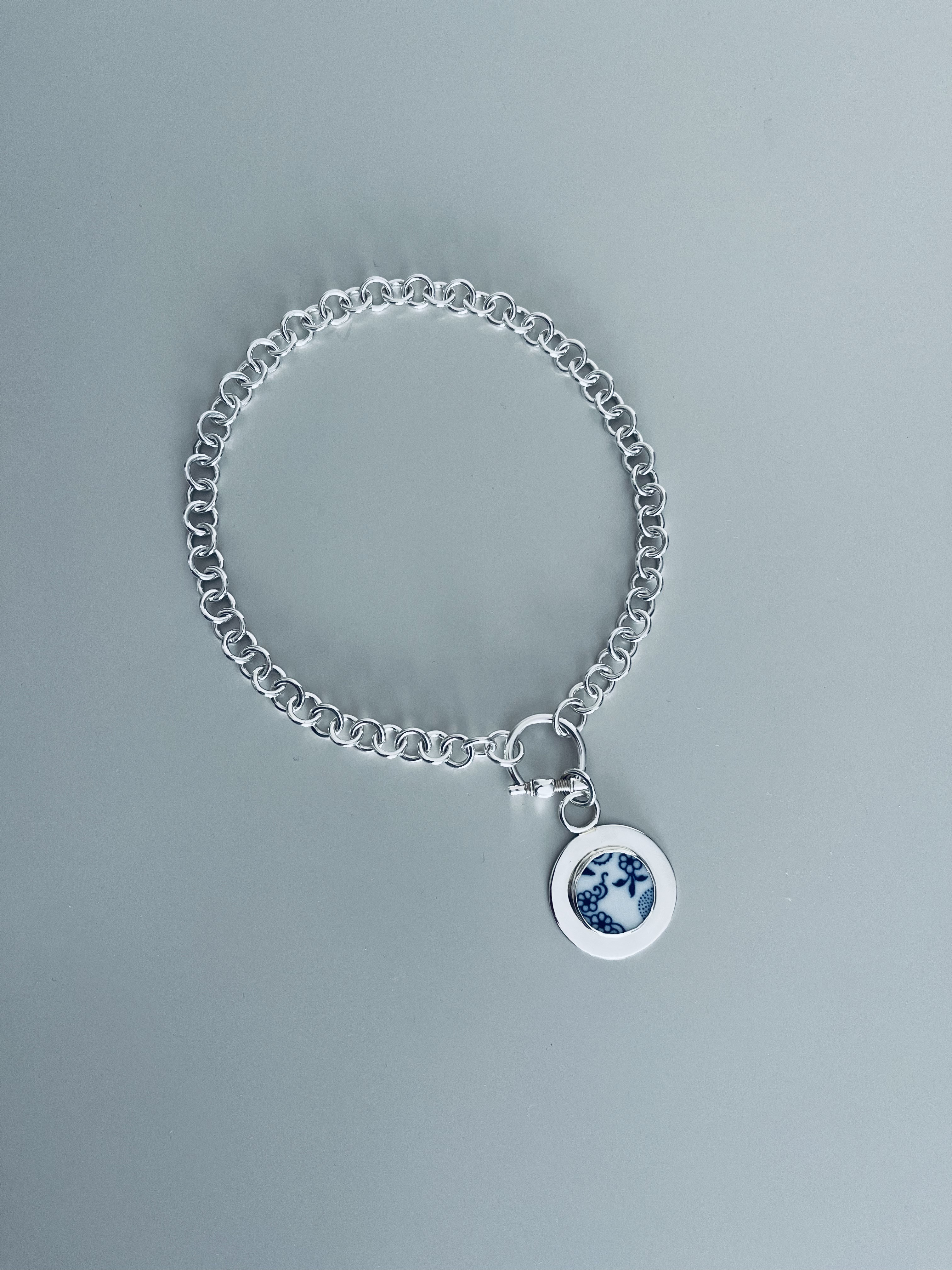 Silver chain bracelet with porcelain charm on a pale blue background