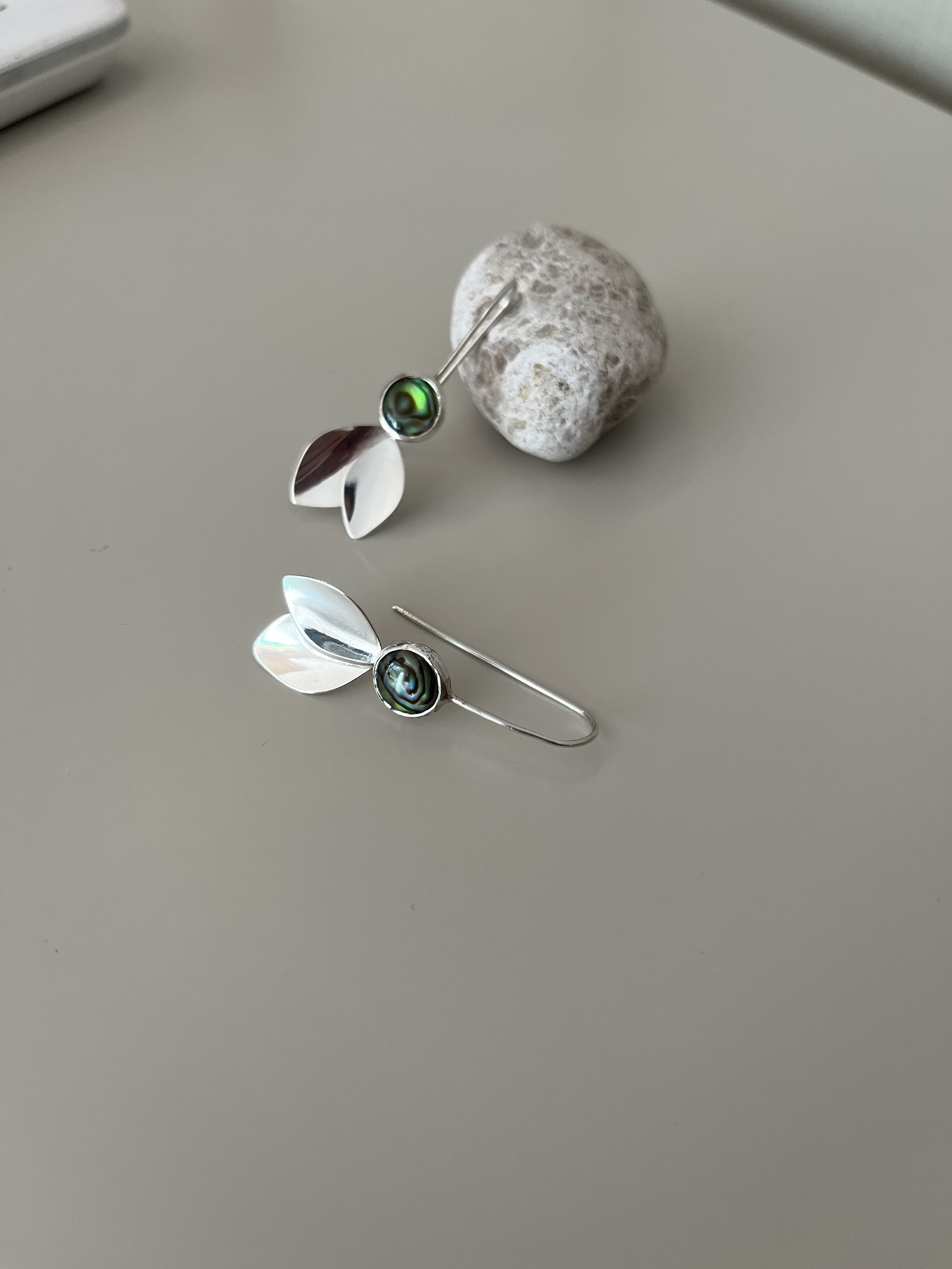 Silver earrings with iridescent stones arranged beside a small stone