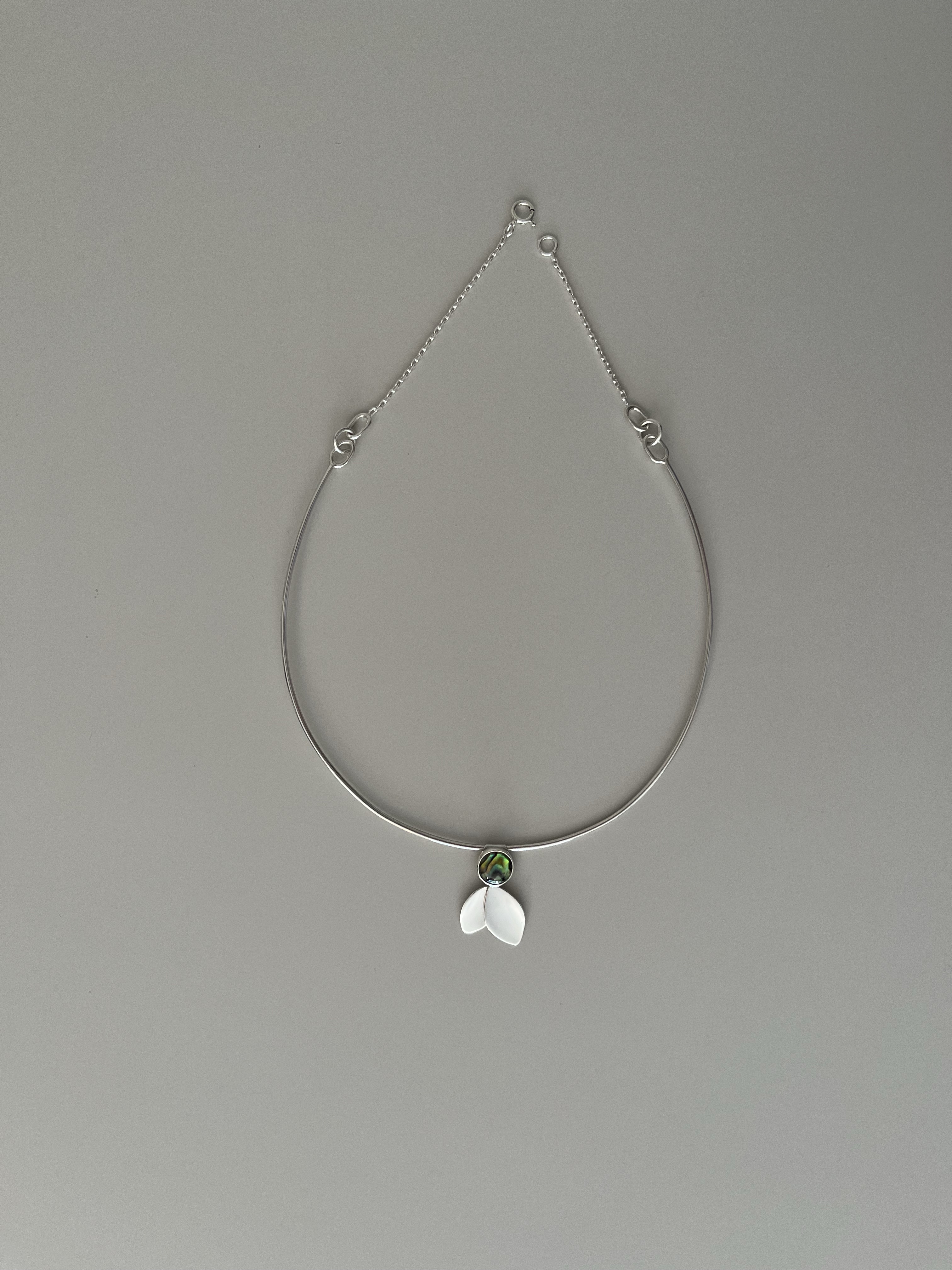 Silver necklace with an iridescent stone and shell-like pendant on a neutral background