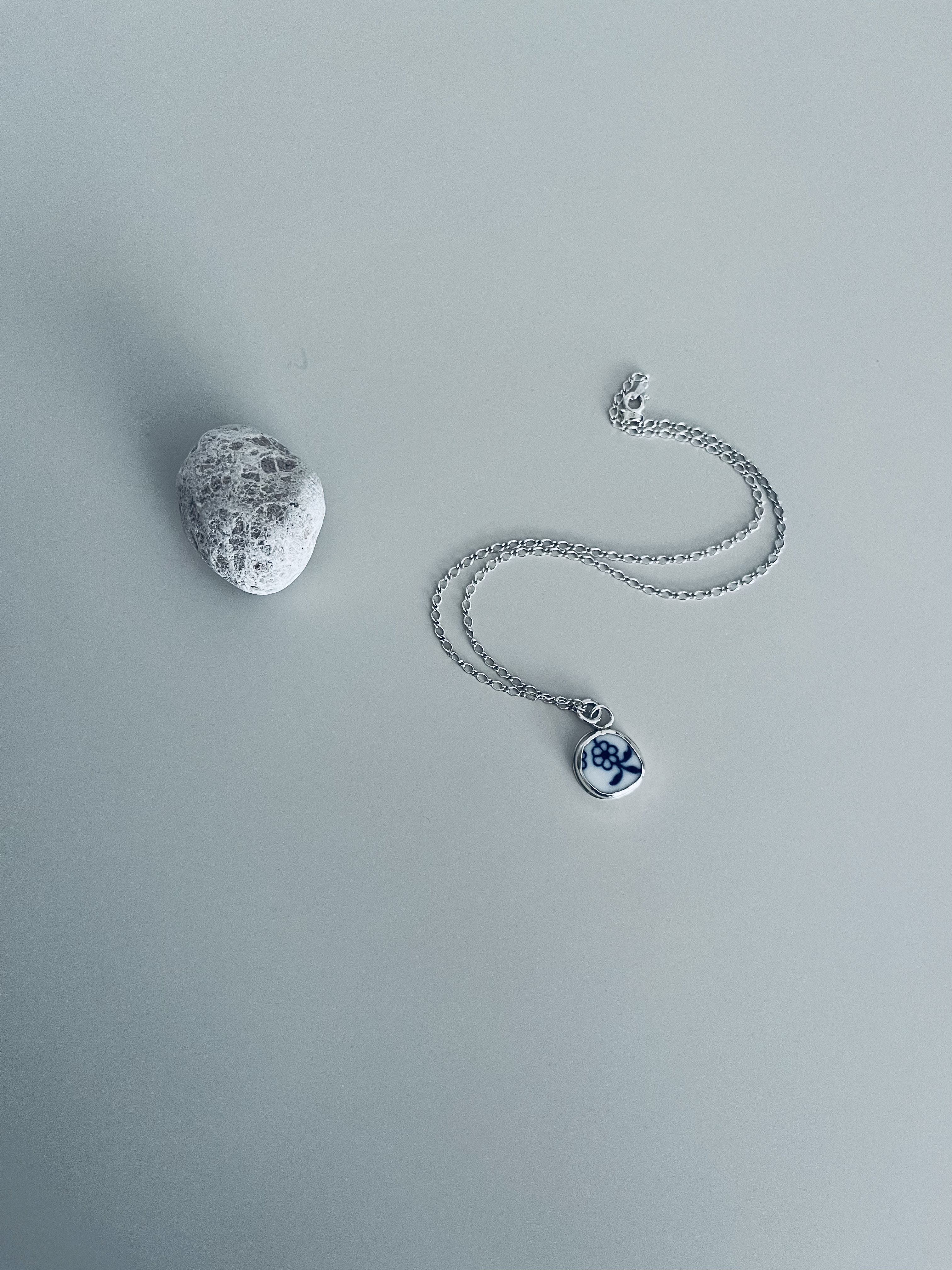Silver porcelain pendant beside a stone on a pale background